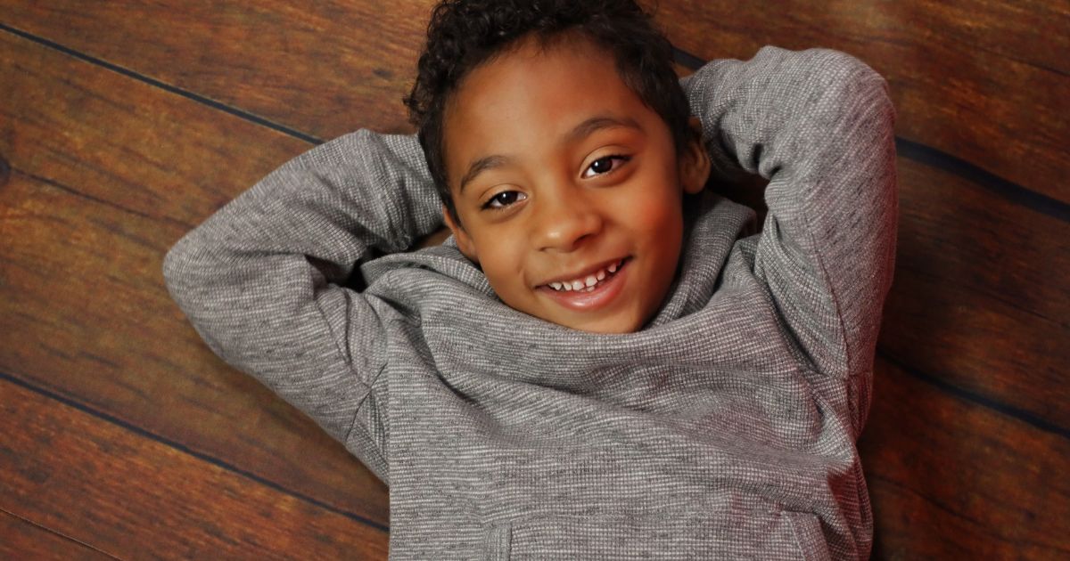 Best Photography Poses For Pictures (From A Pro Photographer) A Young Boy Striking Photography Poses On A Wooden Floor.