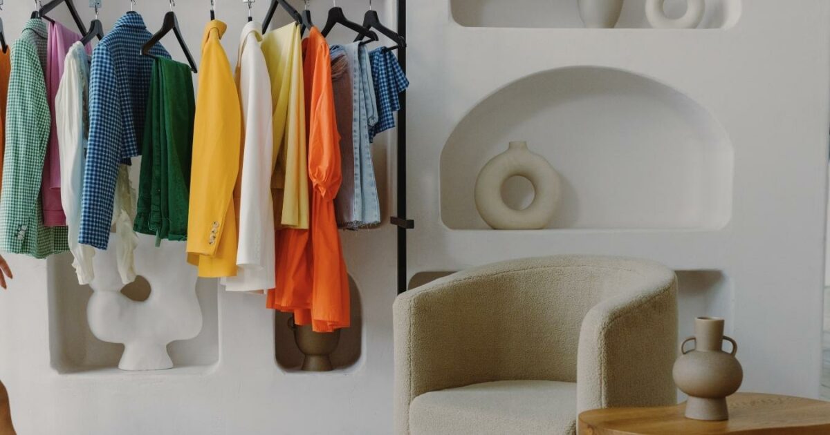 What To Wear To A Photoshoot (The Ultimate Guide) A Woman Is Standing In Front Of A Rack Of Clothes, Contemplating What To Wear For Her Photoshoot.