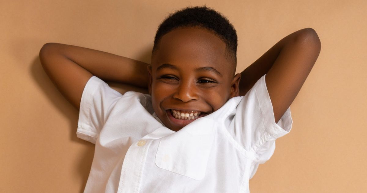 Best Photography Poses For Pictures (From A Pro Photographer) A Young Black Boy Poses On A Beige Background.