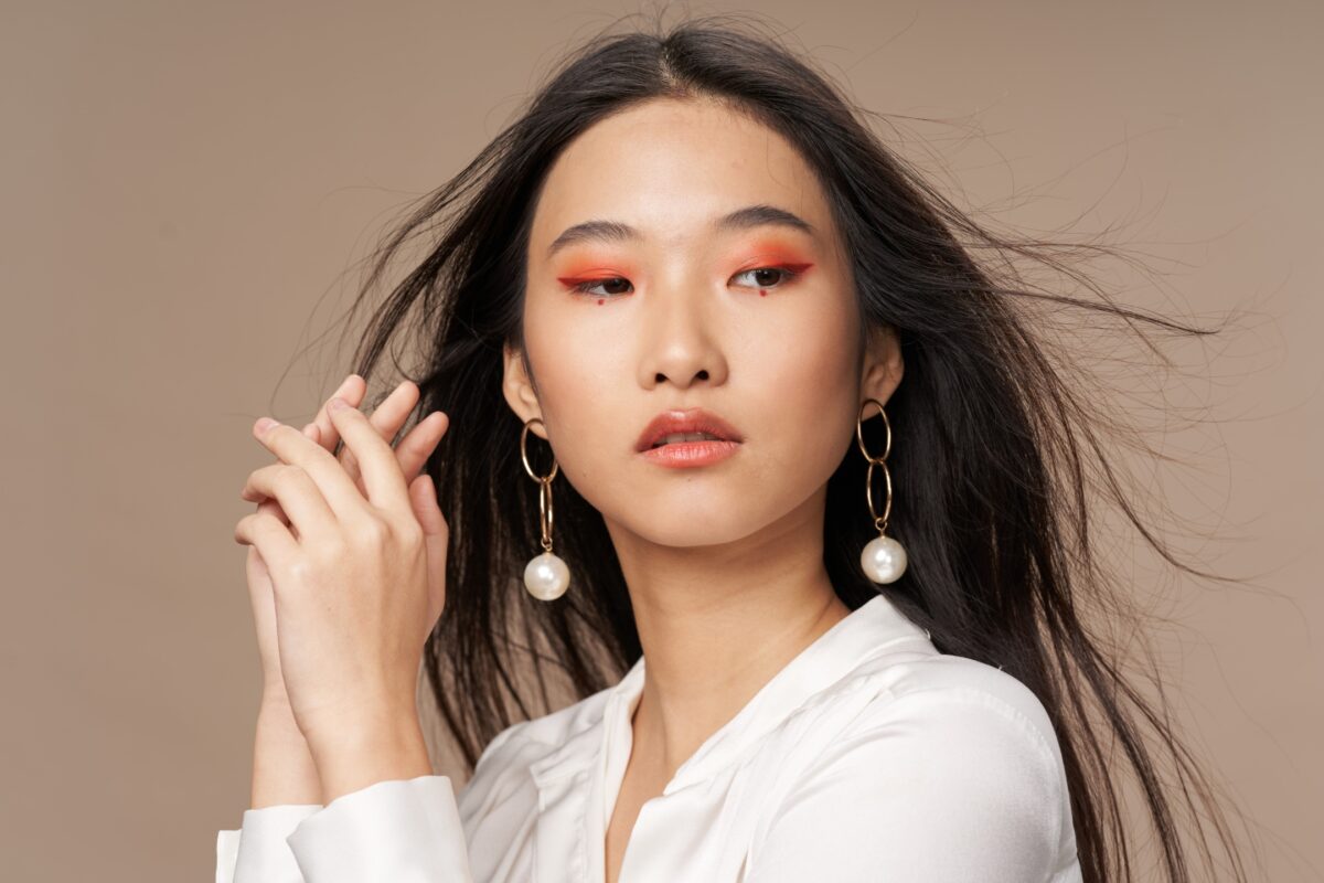 Photography Lighting Setup For Beginners (An Easy Guide) A Young Asian Woman In A White Shirt With Orange Earrings Poses For A Photo Session, While The Photographer Provides Posing Prompts And Guides On What To Say To Clients.