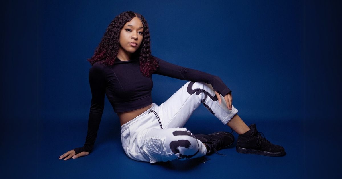 Best Photography Poses For Pictures (From A Pro Photographer) A Woman Posing In A Black Top And White Pants On A Blue Background.