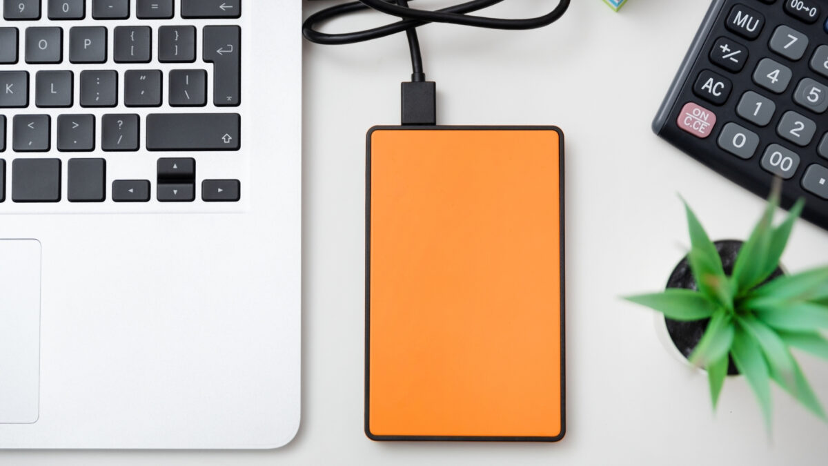 How To Store And Backup Photos Safely An Orange Power Bank Conveniently Placed Next To A Laptop And A Plant, Providing The Perfect Portable Solution To Store And Backup Photos On-The-Go.