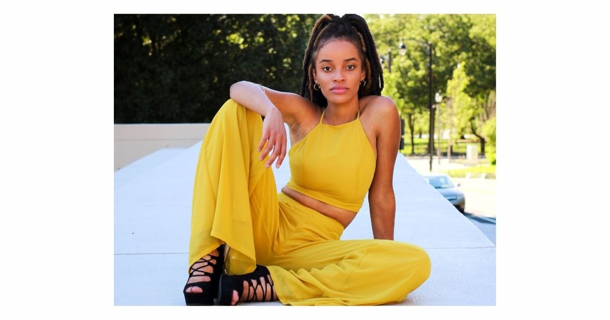 Best Photography Poses For Pictures (From A Pro Photographer) A Woman Poses For A Picture On A Wall In A Yellow Jumpsuit.