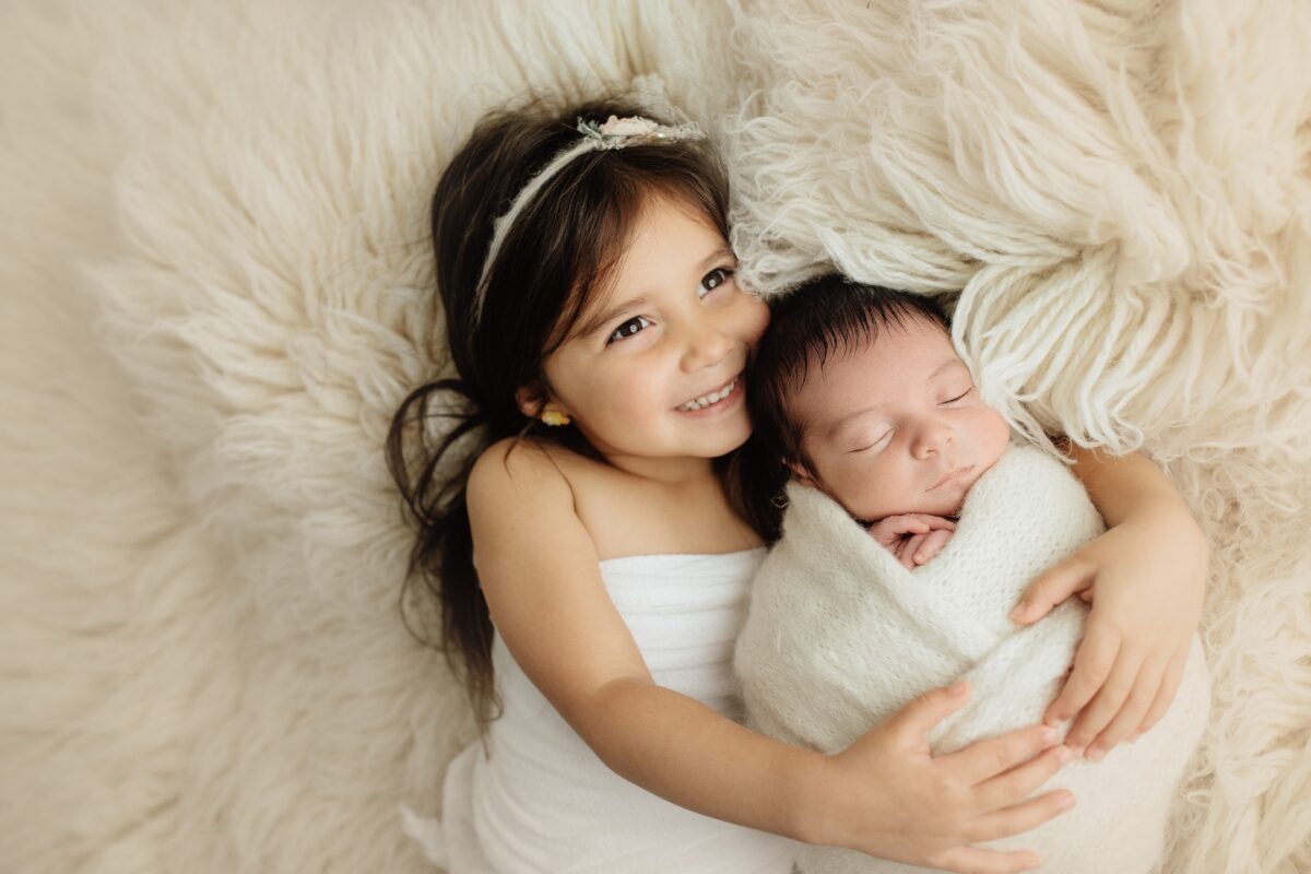 What To Say To Clients During A Photo Session: With Prompts A Little Girl Poses With Her Newborn, Wrapped Up In A Blanket, During A Heartwarming Photo Session.