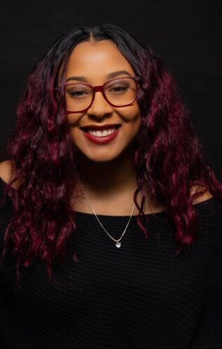 About A Black Woman With Red Hair And Glasses Smiling.