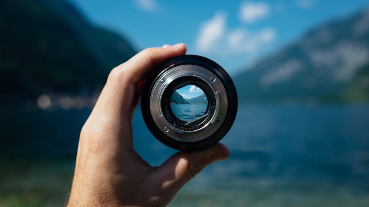 How To Learn And Improve From Mistakes As A Photographer A Person Making Mistakes As A Photographer While Holding Up A Camera Lens With A Lake In The Background.