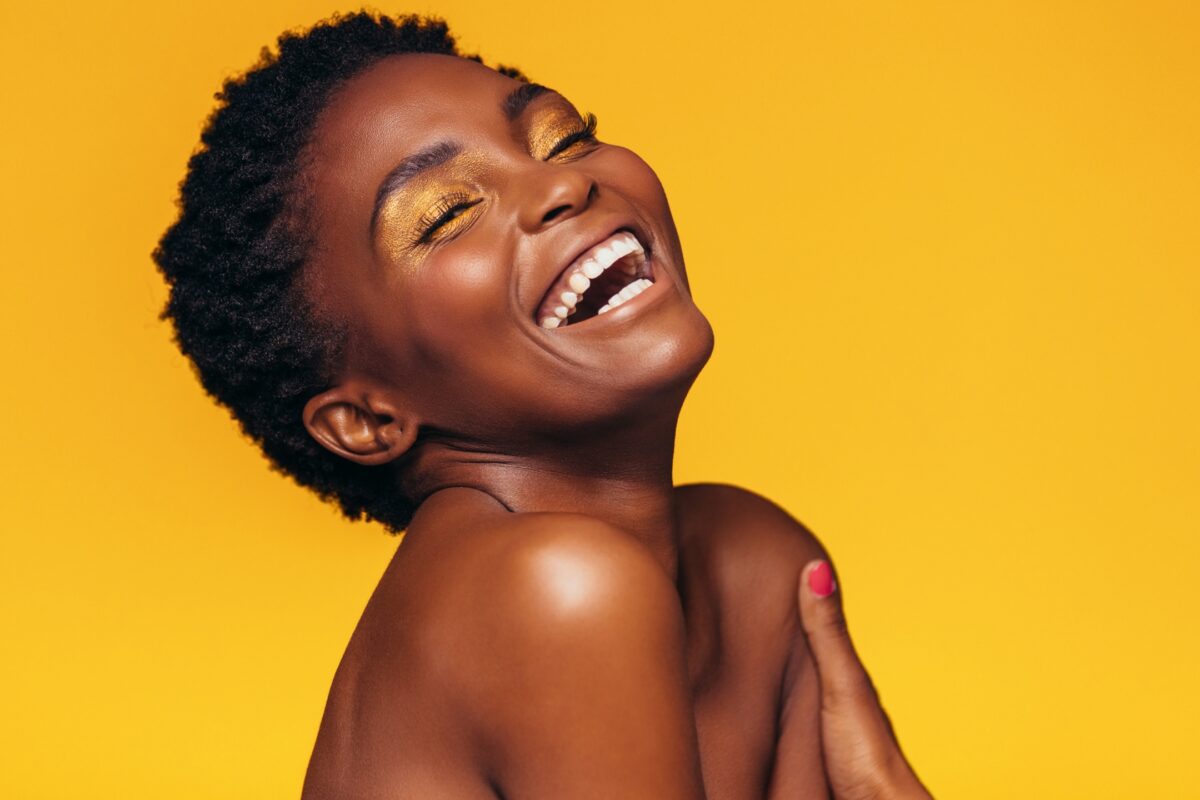 What To Say To Clients During A Photo Session: With Prompts A Young Black Woman Laughing On A Vibrant Yellow Background, Guided By Posing Prompts During The Photo Session.
