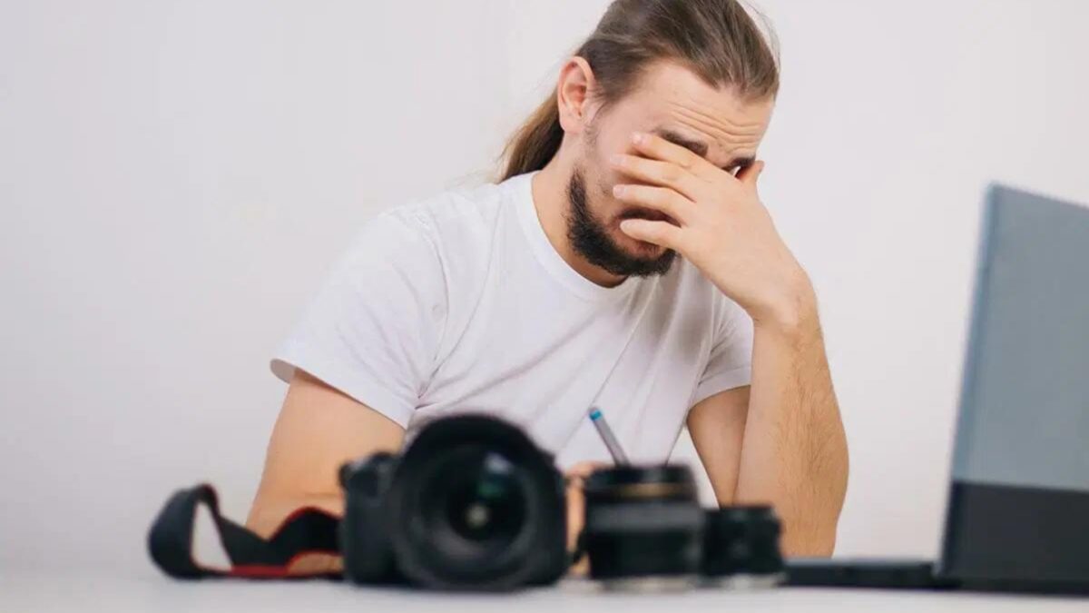 The Best Cloud Storage For Photos A Man Covering His Face In Frustration While Sitting At A Desk With A Laptop, Reflecting On His Mistakes As A Photographer.