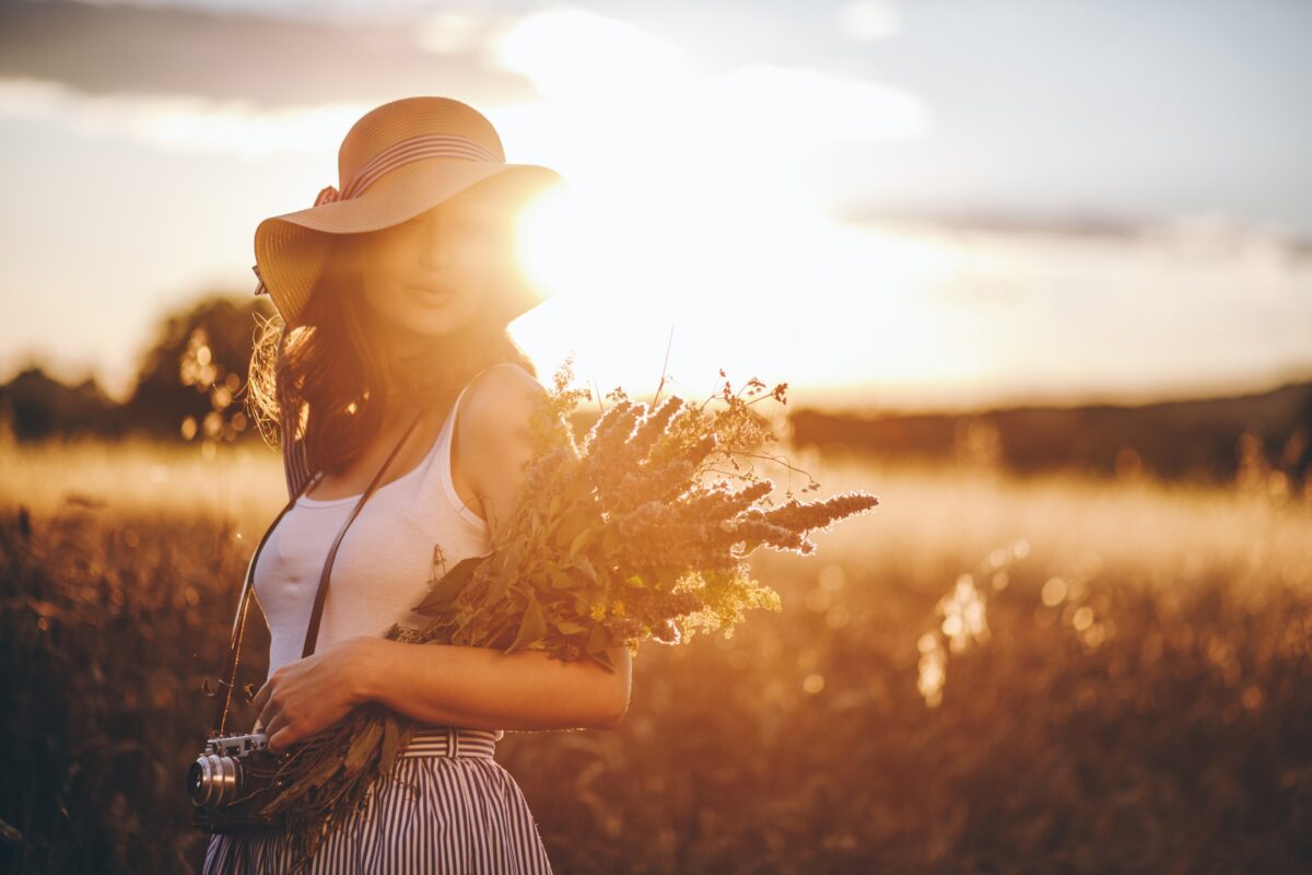 A Simple Guide To Harsh Sunlight Photography A Woman In A Hat Holding Flowers In A Field During Sunset, Captured With The Warm Glow Of Harsh Sunlight.