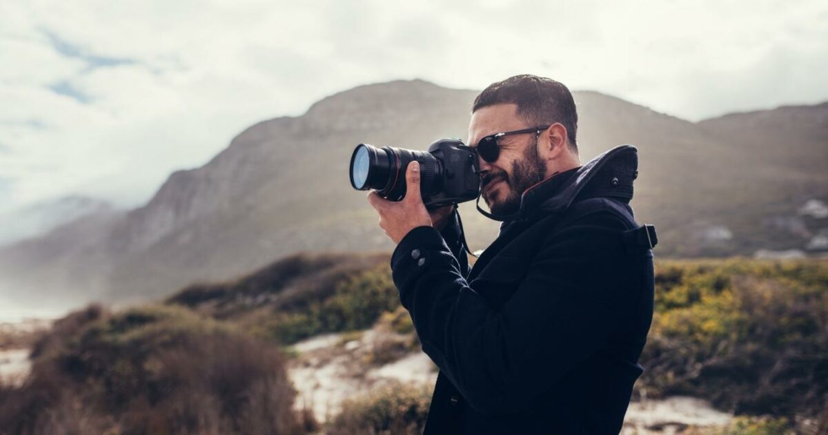 What Is A Photo Essay In Photography (13 Examples You Can Try) A Man Is Capturing A Picture With His Camera On The Beach For A Photo Essay.