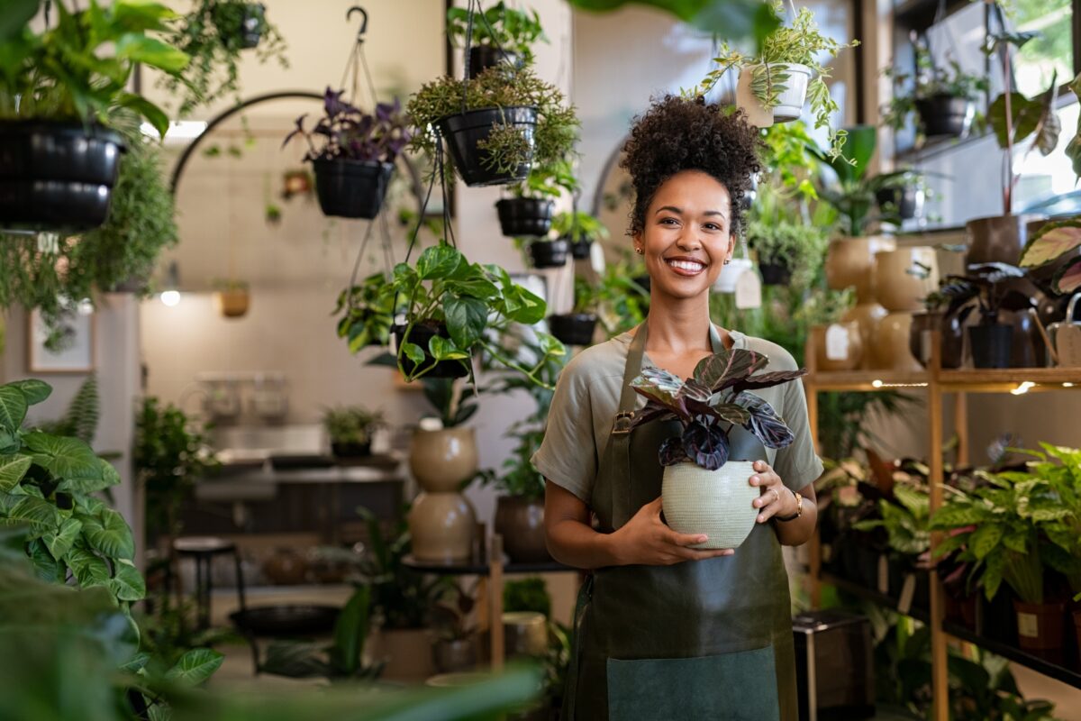 Why Photography Is Important In Business And Life A Woman In An Apron Is Holding A Potted Plant In A Store, Showcasing Why Photography Is Important.